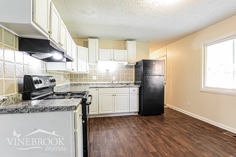 A kitchen with a black refrigerator and a granite counter top.