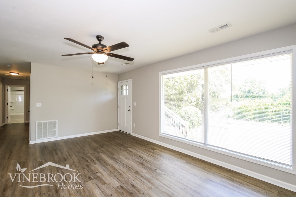 A room with a ceiling fan and a window overlooking a tree.