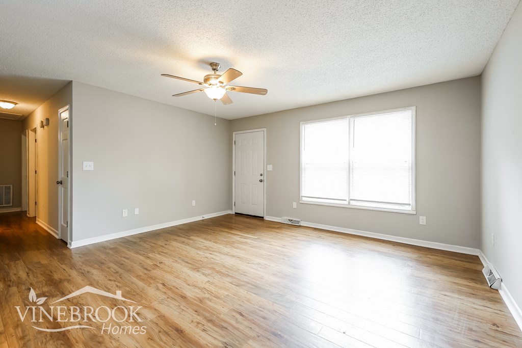 an empty living room with a ceiling fan and a window