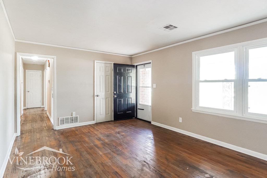a living room with a hardwood floor and a door to a hallway with windows