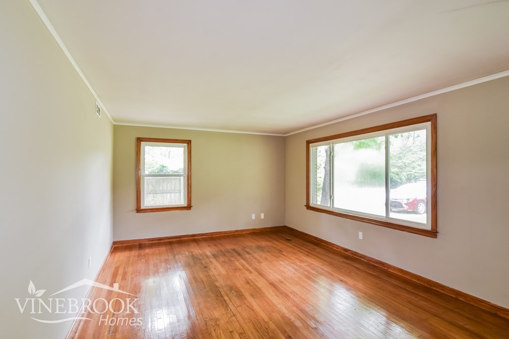 an empty living room with wood floors and two windows