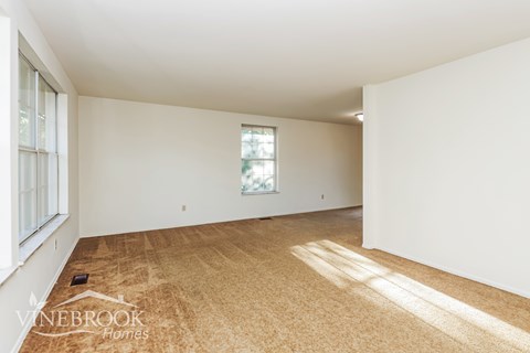 a living room with white walls and carpet and a window