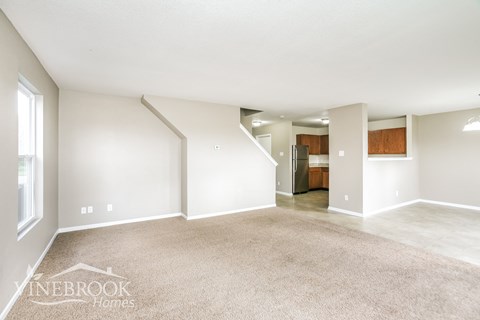 the living room and kitchen of an apartment with white walls and carpet