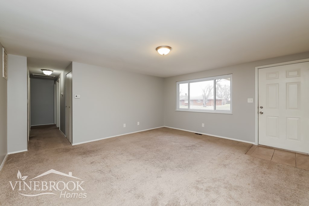 A spacious room with a carpeted floor and a window letting in natural light.
