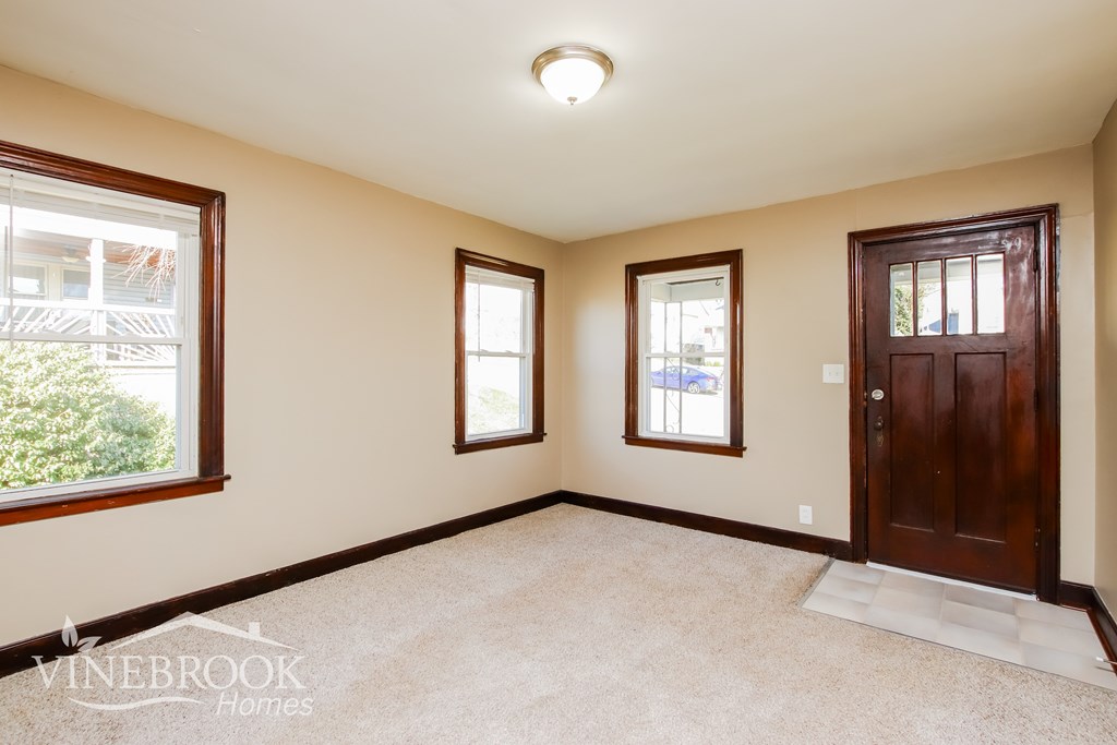 A room with a carpeted floor, a door, and two windows.