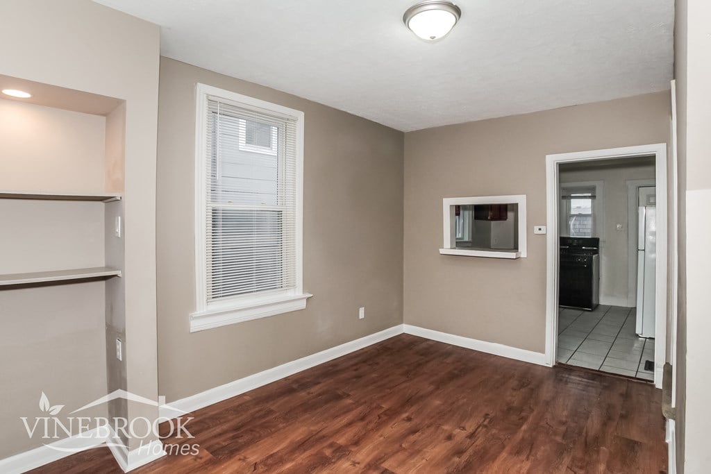 A room with a window and a door leading to a kitchen.