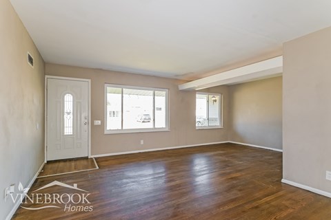 A room with a door, two windows and a wooden floor.