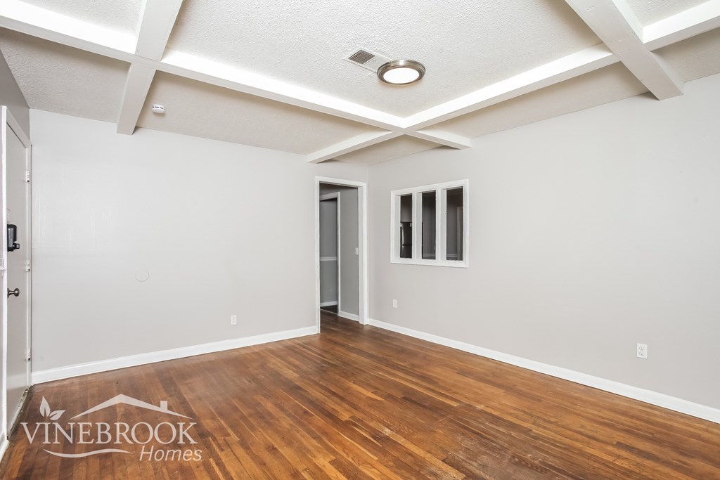 A room with wood flooring and white walls, with a door and a window.