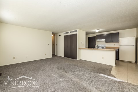 A spacious room with a kitchenette and a door leading to another room.