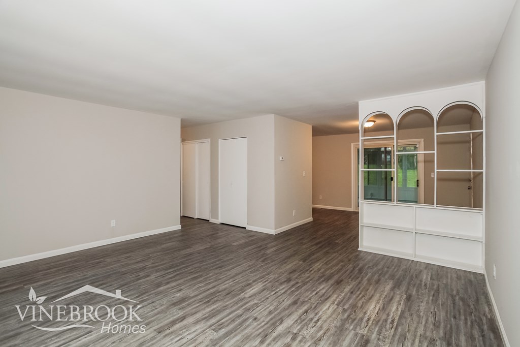 A spacious room with wood flooring and white walls, with a logo for Vinebrook Homes in the bottom left corner.