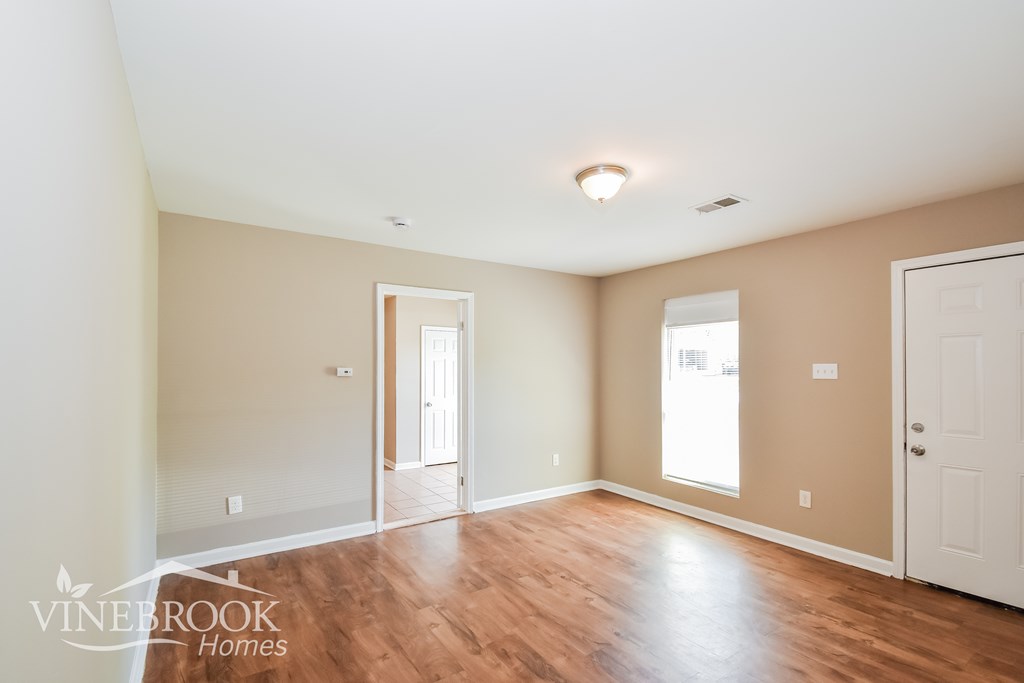 A room with wood floors and white walls, with a door on the right and a window on the left.
