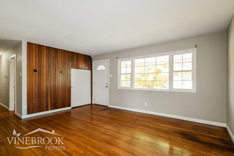 A room with wood flooring and a window with a view of trees.
