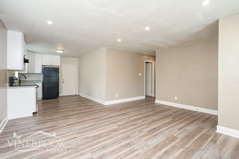 A spacious room with wooden flooring and a kitchen area with white cabinets and appliances.