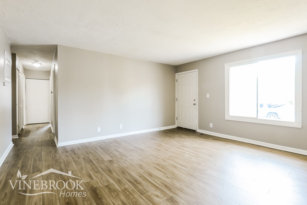 A room with wooden floors and white walls, with a window on the right wall.