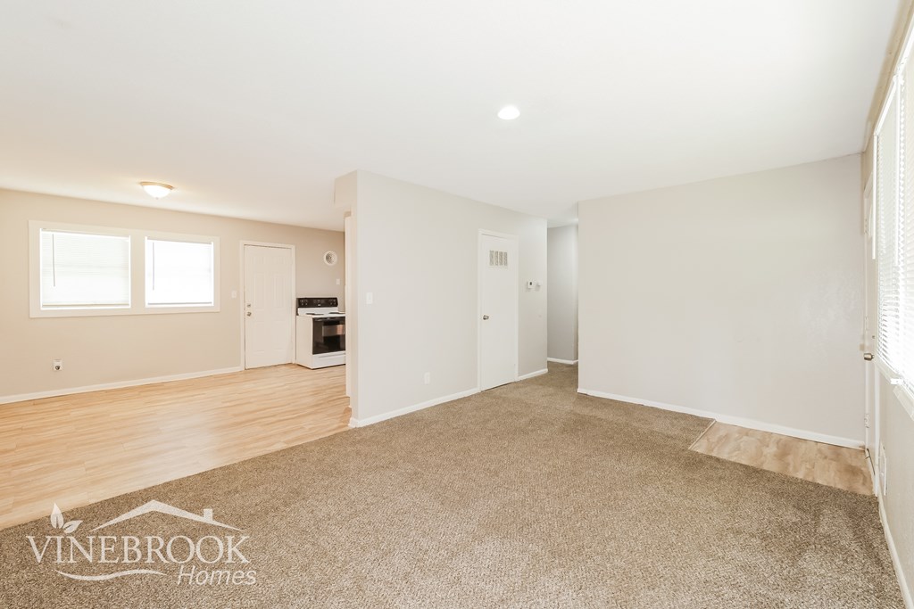A spacious room with a carpeted floor and a window on the left side.