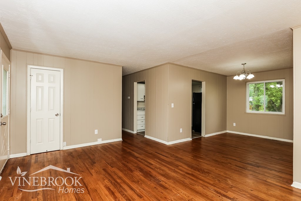 A spacious room with wood flooring and a large window.