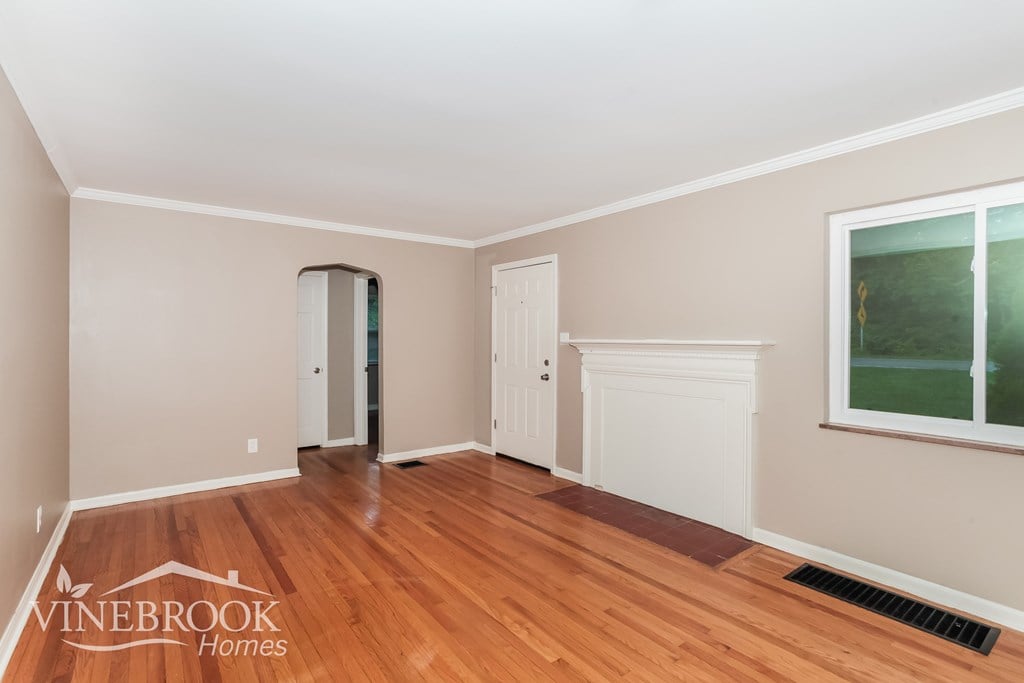 A room with wood flooring and a window showing greenery outside.