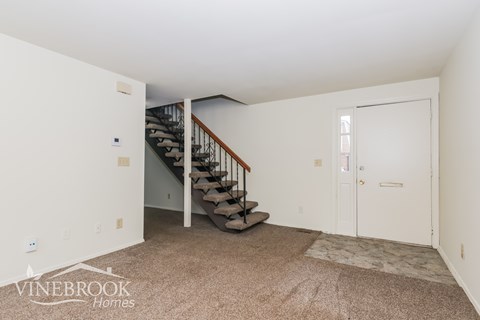 A carpeted room with a staircase leading to the second floor.