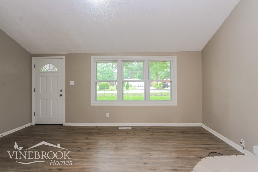 A room with a white door and a window with a view of a green lawn.