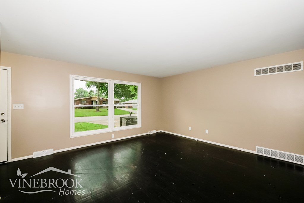 A room with a large window and a view of a lawn and trees.