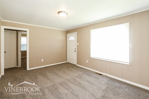 A room with a carpeted floor and a window with white blinds.
