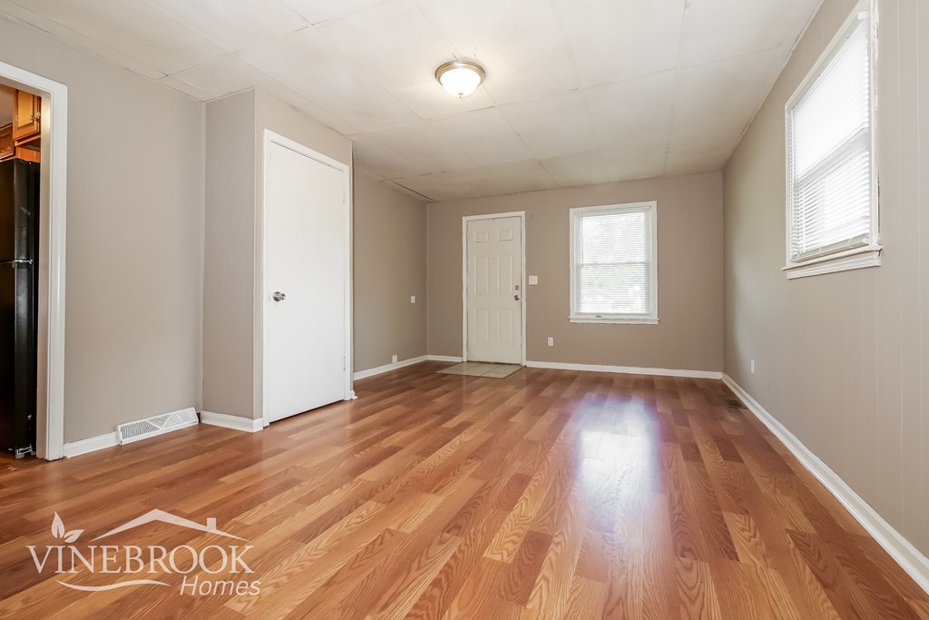 A room with wooden floors and white walls, with a window on the right wall.