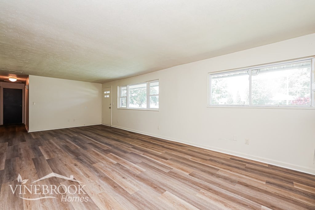 A room with wooden flooring and two windows.