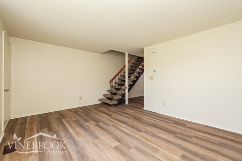 A room with wooden flooring and a staircase in the background.
