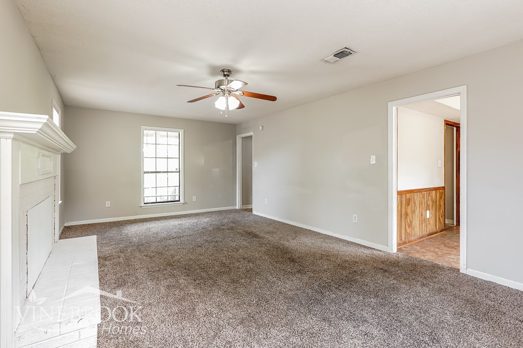 A spacious room with a ceiling fan and a door leading to another room.