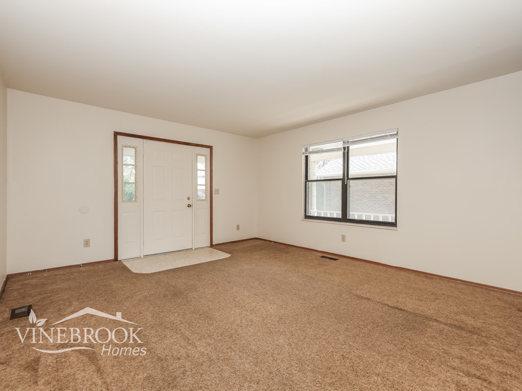 A room with a carpeted floor, a door, and a window.