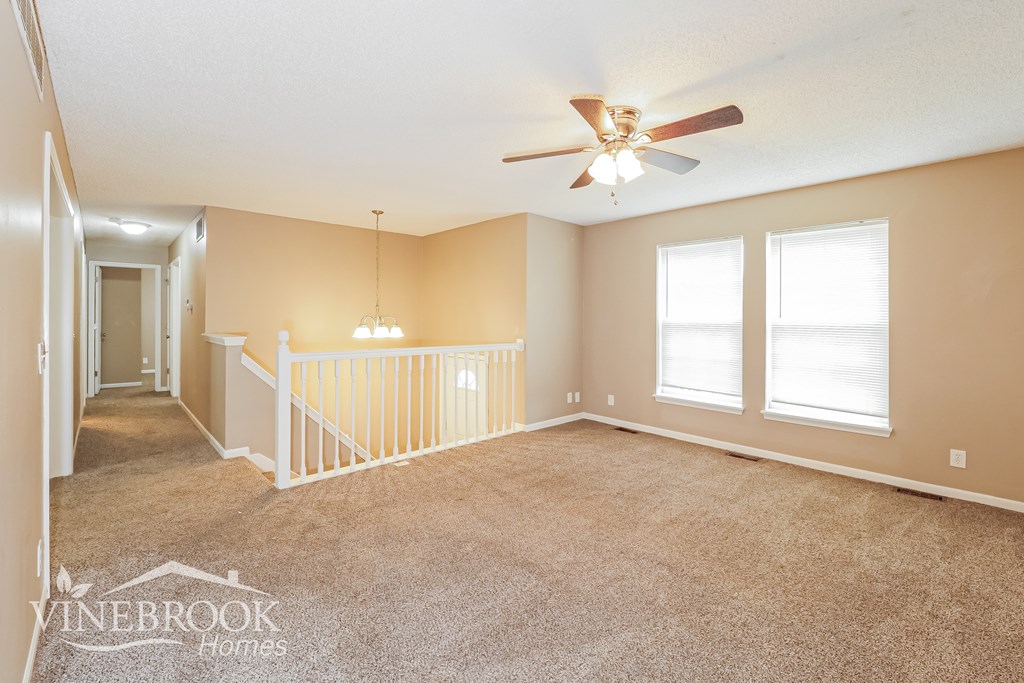 A spacious room with a carpeted floor, a ceiling fan, and a staircase leading to another room.