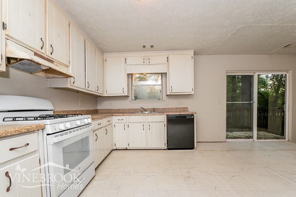 a kitchen with white cabinets and a white stove and a black dishwasher