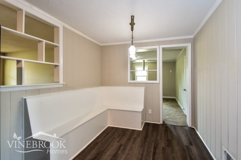 a dining room with a white bench and shelves and a hallway