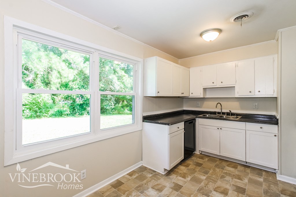 a kitchen with white cabinets and black counter tops and a window