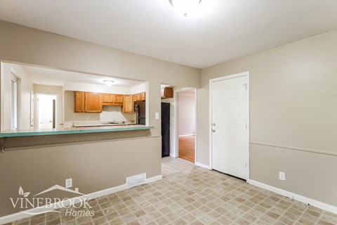 A room with a kitchen area in the background and a doorway leading to another room.