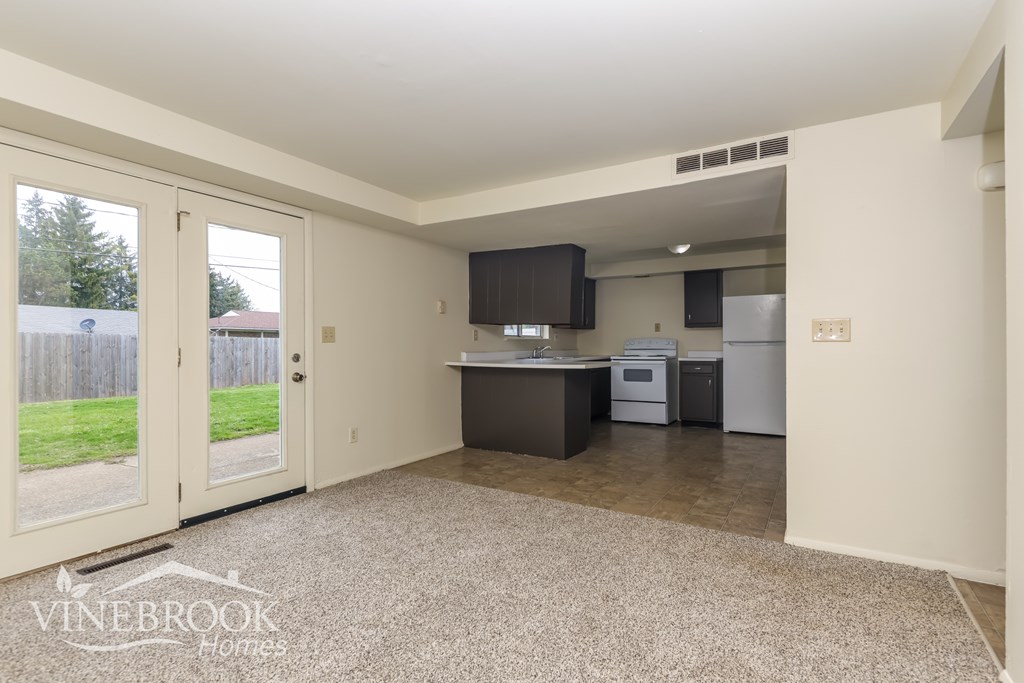 A clean, empty room with a kitchenette and a window with a view of a fence and trees.