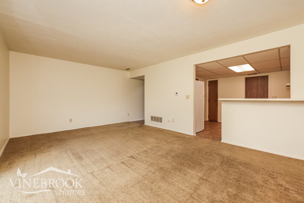 A large empty room with a carpeted floor and a doorway leading to another room.