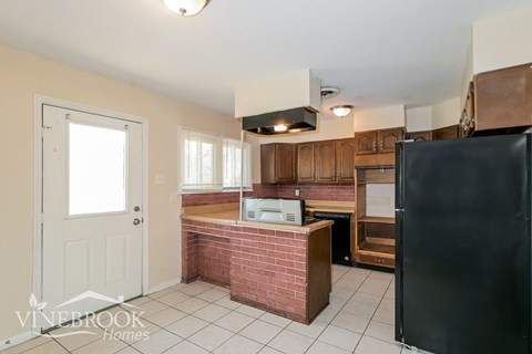 A kitchen with a black refrigerator and wooden cabinets.