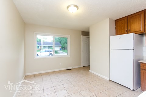 A white refrigerator sits in a kitchen with a window showing a car and house outside.