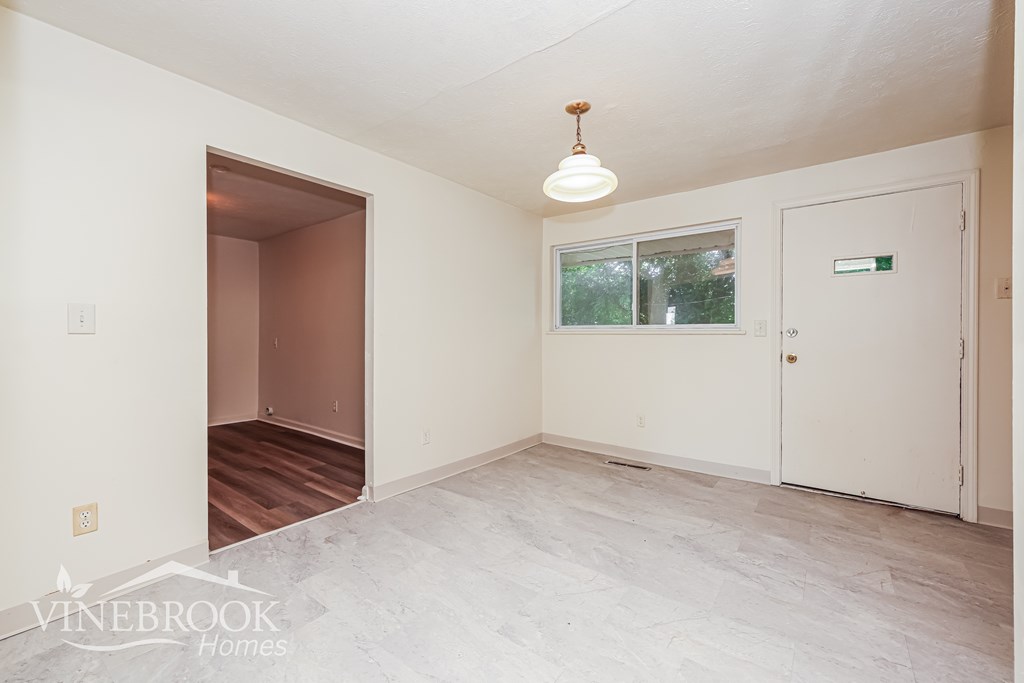 A room with a white door and a window with a view of trees outside.