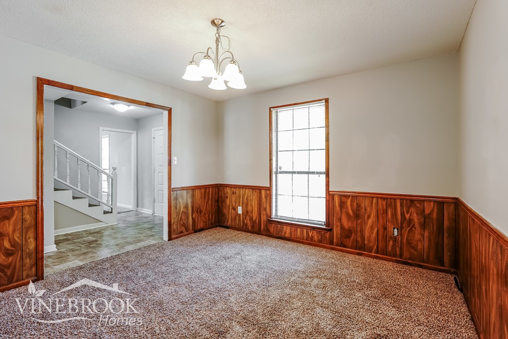 A room with a carpeted floor and a chandelier hanging from the ceiling.