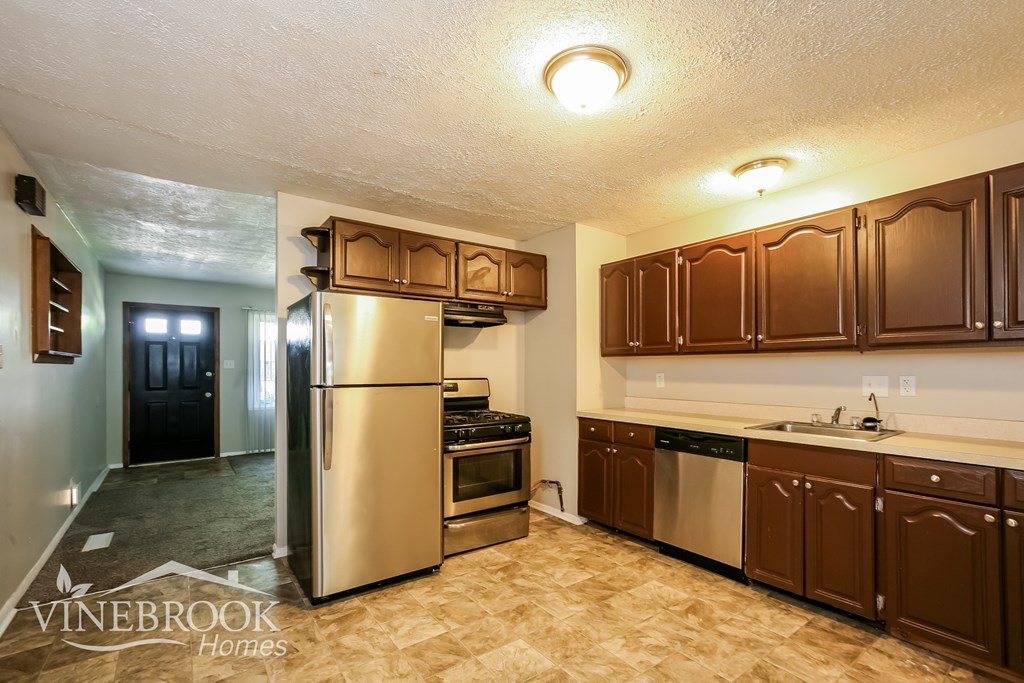 A kitchen with a refrigerator, oven, sink and cabinets.