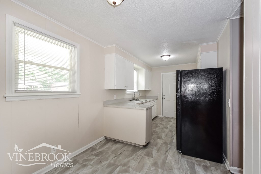 a white kitchen with a black refrigerator and a window