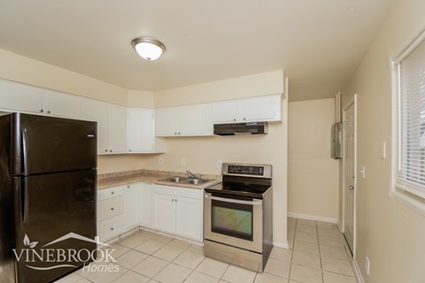 A kitchen with a black refrigerator and white cabinets.