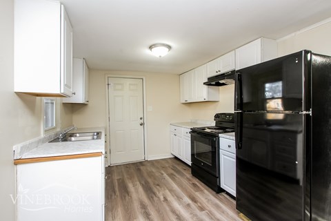 A black refrigerator is in the corner of a kitchen with white cabinets.