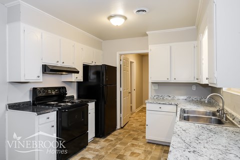 A kitchen with white cabinets and a black refrigerator.