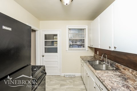 A kitchen with a black fridge and a sink with a granite counter top.