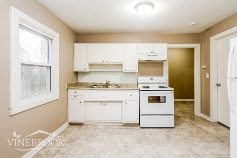 A kitchen with white cabinets and appliances in a Vinebrook Homes model.