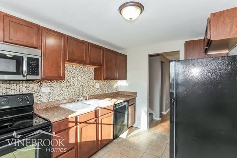 A kitchen with brown cabinets and a black refrigerator.