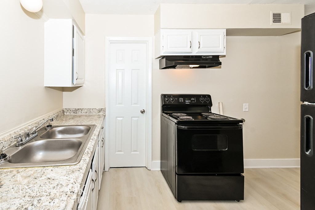 A black stove top oven and black refrigerator in a kitchen with a white door.